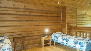Ett rum inrett som en stuga, med träväggar och trägolv, två enkelsängar med blommigt sänglinne, ett litet träbord vid sängen med en lampa och en träbänk.
