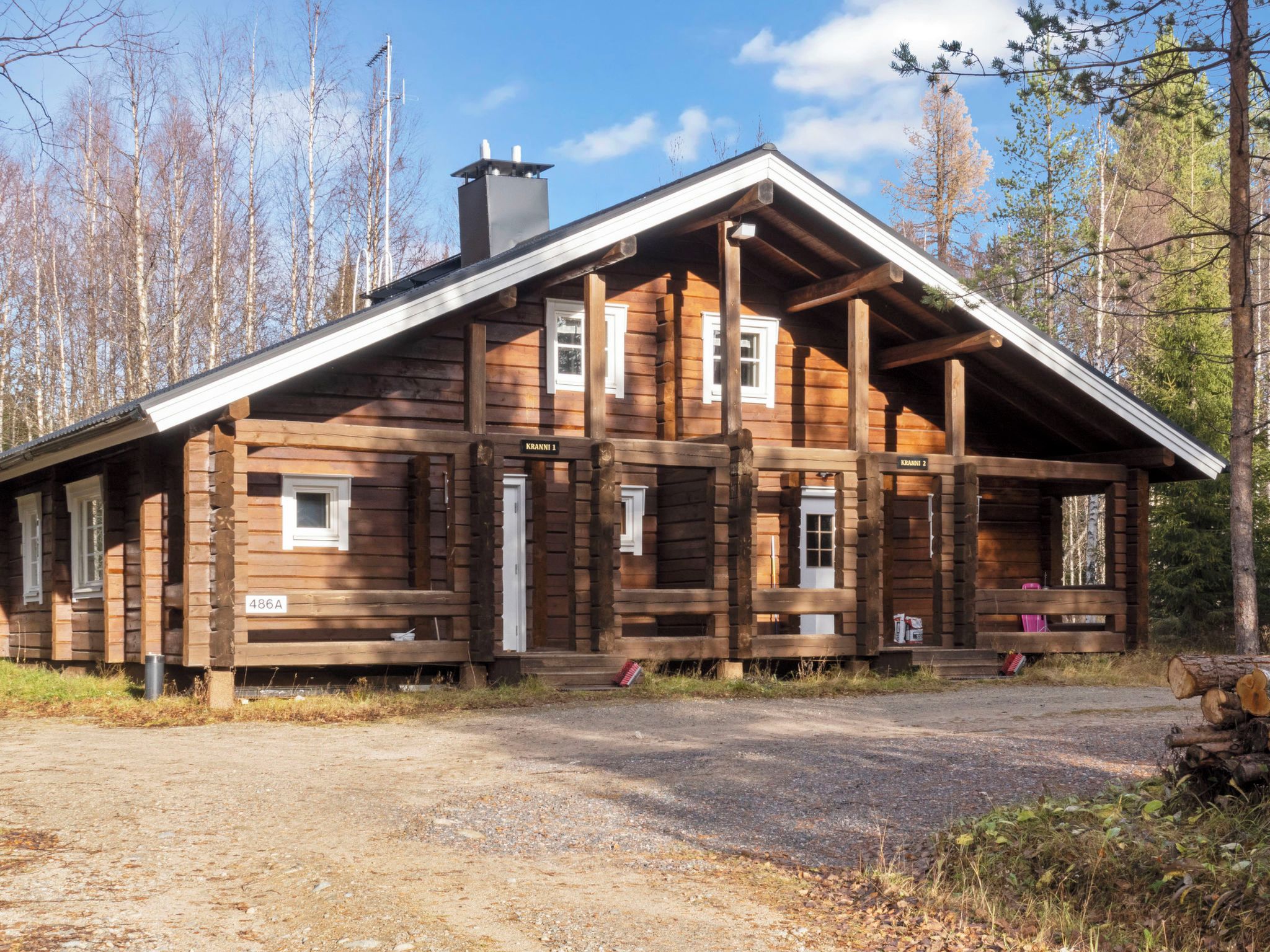 En stuga av trä med ett sadeltak, en skorsten och en veranda med bänkar.