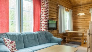 A cozy cabin interior with a blue sofa, a wooden table, and a television mounted on the wall. - Kranni 2 by Interhome (Pudasjärvi)