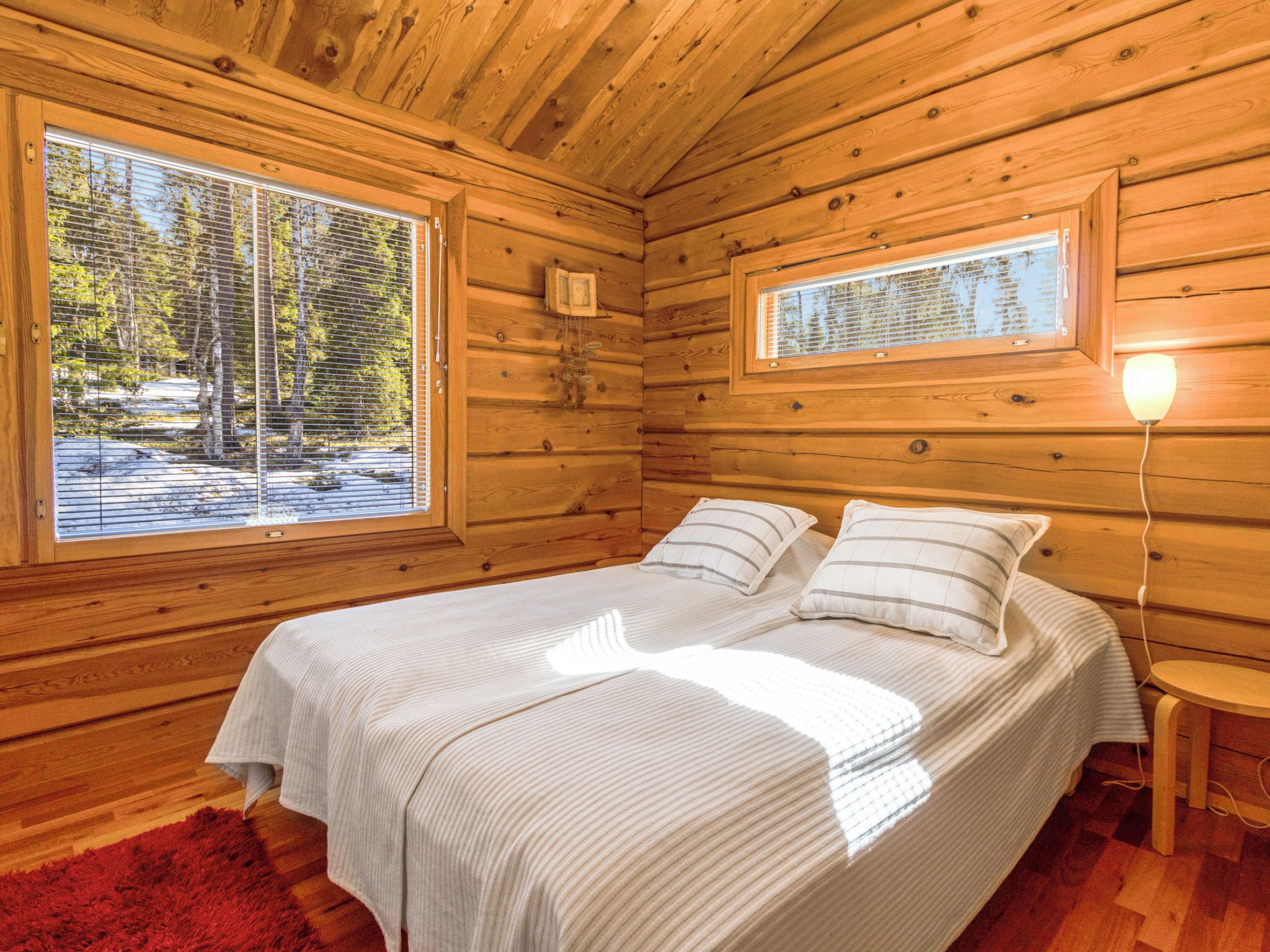 Una camera in una baita di legno con un letto, due finestre e un comodino.
