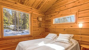 Ein Holzhütten-Zimmer mit Bett, zwei Fenstern und einem Nachttisch.