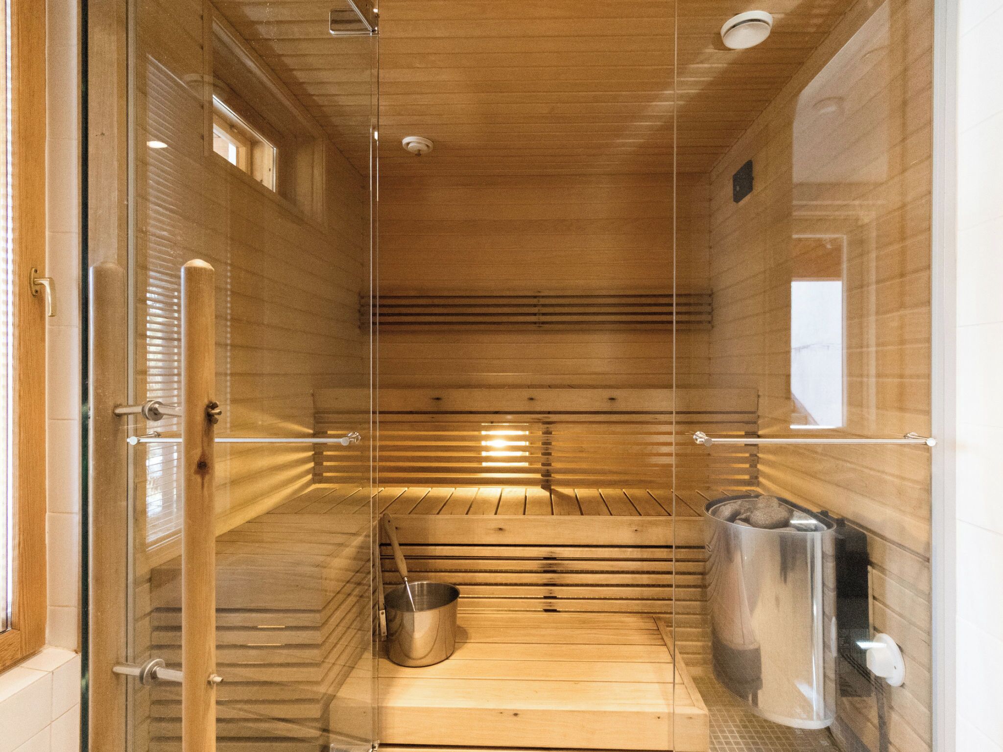 A sauna with a wooden bench, a metal bucket, and a trash can.