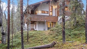 Eine zweistöckige Holzblockhütte mit einem Balkon, umgeben von Wald.