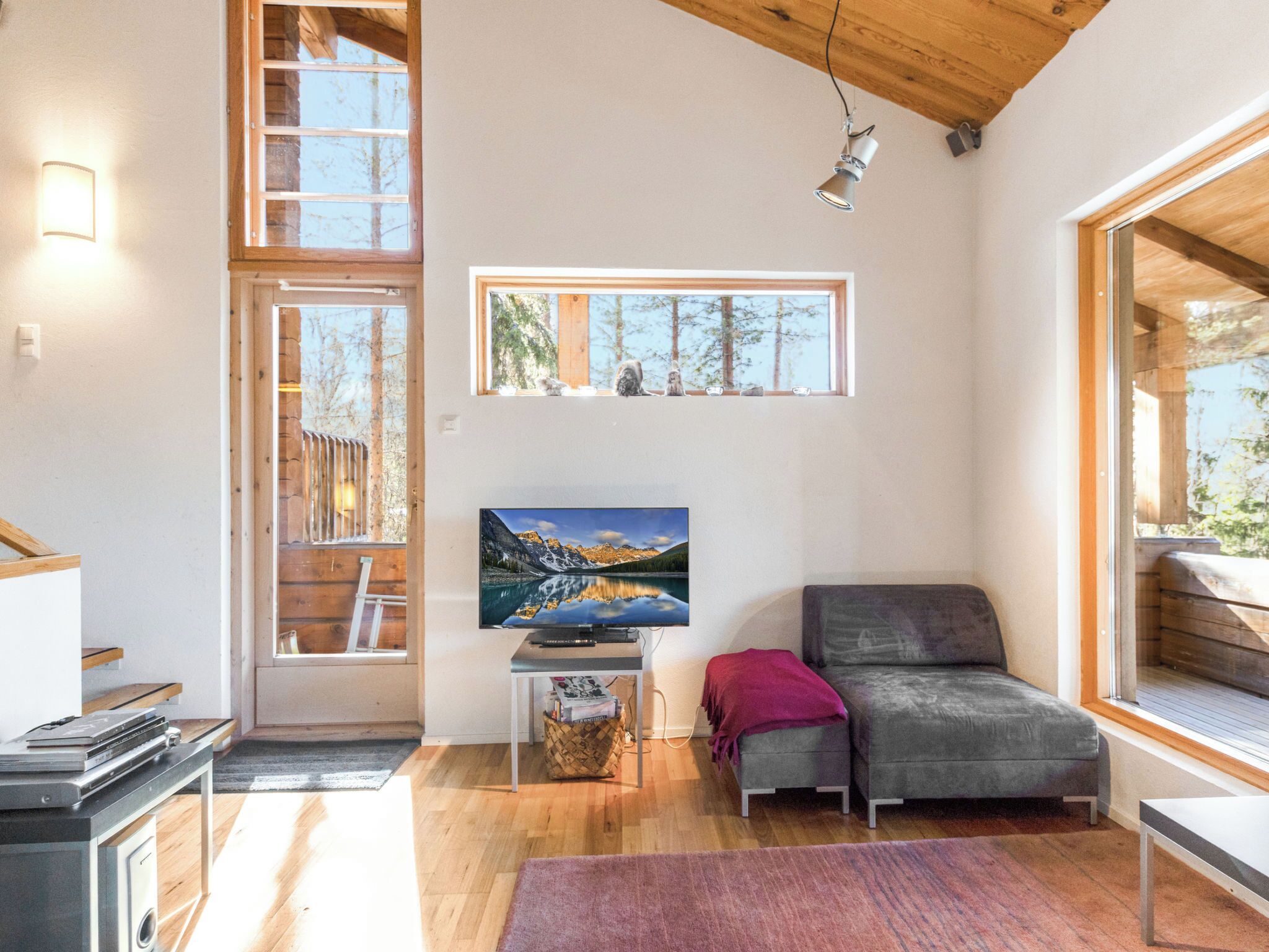 Un interno moderno con soffitto in legno, un'ampia finestra, una televisione a schermo piatto, un divano e un tavolino.