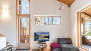 Ein modernes Interieur mit Holzbalkendecke, einem großen Fenster, einem Flachbildfernseher, einer Couch und einem kleinen Tisch.