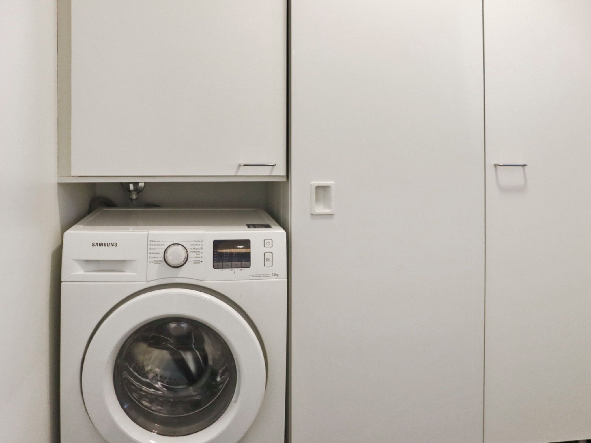 A Samsung washing machine in a laundry room with a white cabinet above it.
