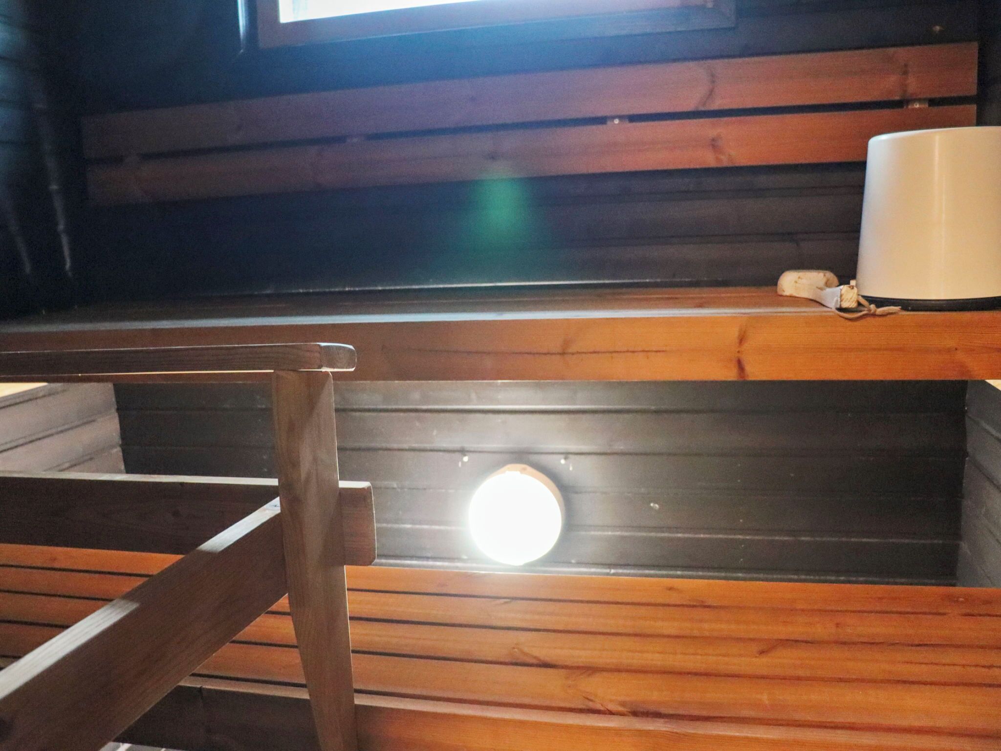 A wooden bench with a circular window, a white mug, and a wooden table.