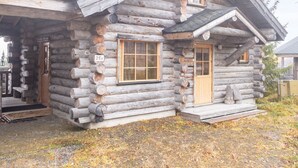 A log cabin with a porch, a chimney, and a window with shutters.
