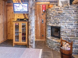 A wooden interior with a stone fireplace, a television mounted on the wall, and a cabinet with glass doors.