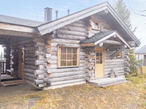 A log cabin with a front porch, a chimney, and a window with shutters.