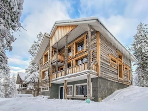 A multi-story log cabin with a balcony, surrounded by snow-covered trees. - Pyhän kivi by Interhome (Pelkosenniemi)