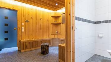 A sauna room with wooden benches, a wooden stool, and a white tiled wall.