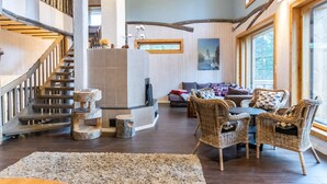 Un espacio habitable amplio con una escalera de madera, chimenea y mobiliario de mimbre.