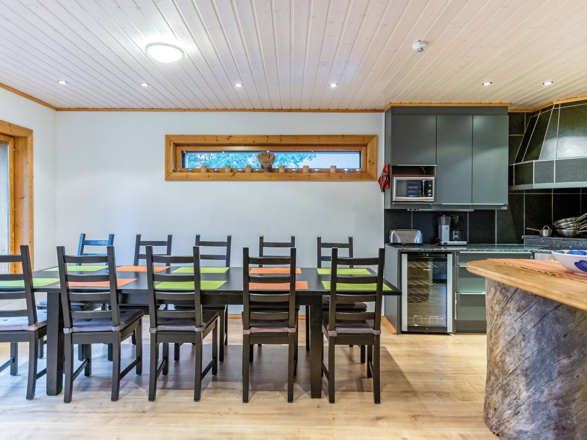 A modern kitchen with a dining area, wooden ceiling, and a window with a view.