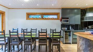 A modern kitchen with a dining area, wooden ceiling, and a window with a view.