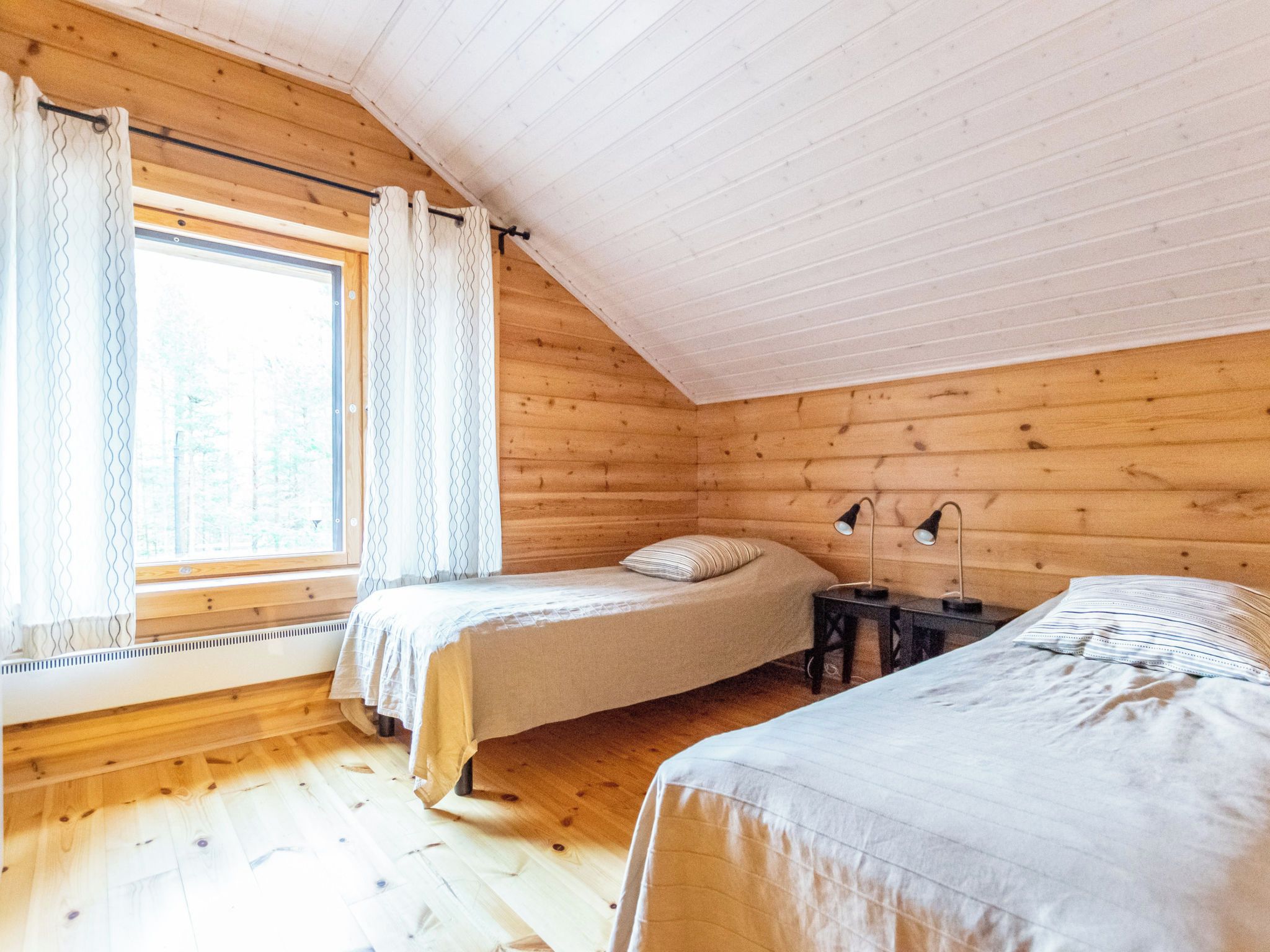 Una cabaña con habitación en un altillo, paredes de madera, un ventanal con cortinas y una cama con almohada.