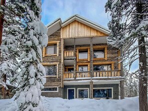 A multi-story log cabin with a balcony, surrounded by snow-covered trees.
