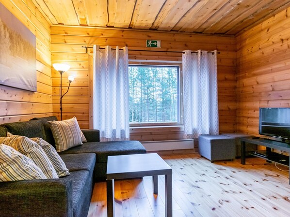 Interior acogedor de una cabaña con un sofá, una mesita, un televisor y una ventana con cortinas.