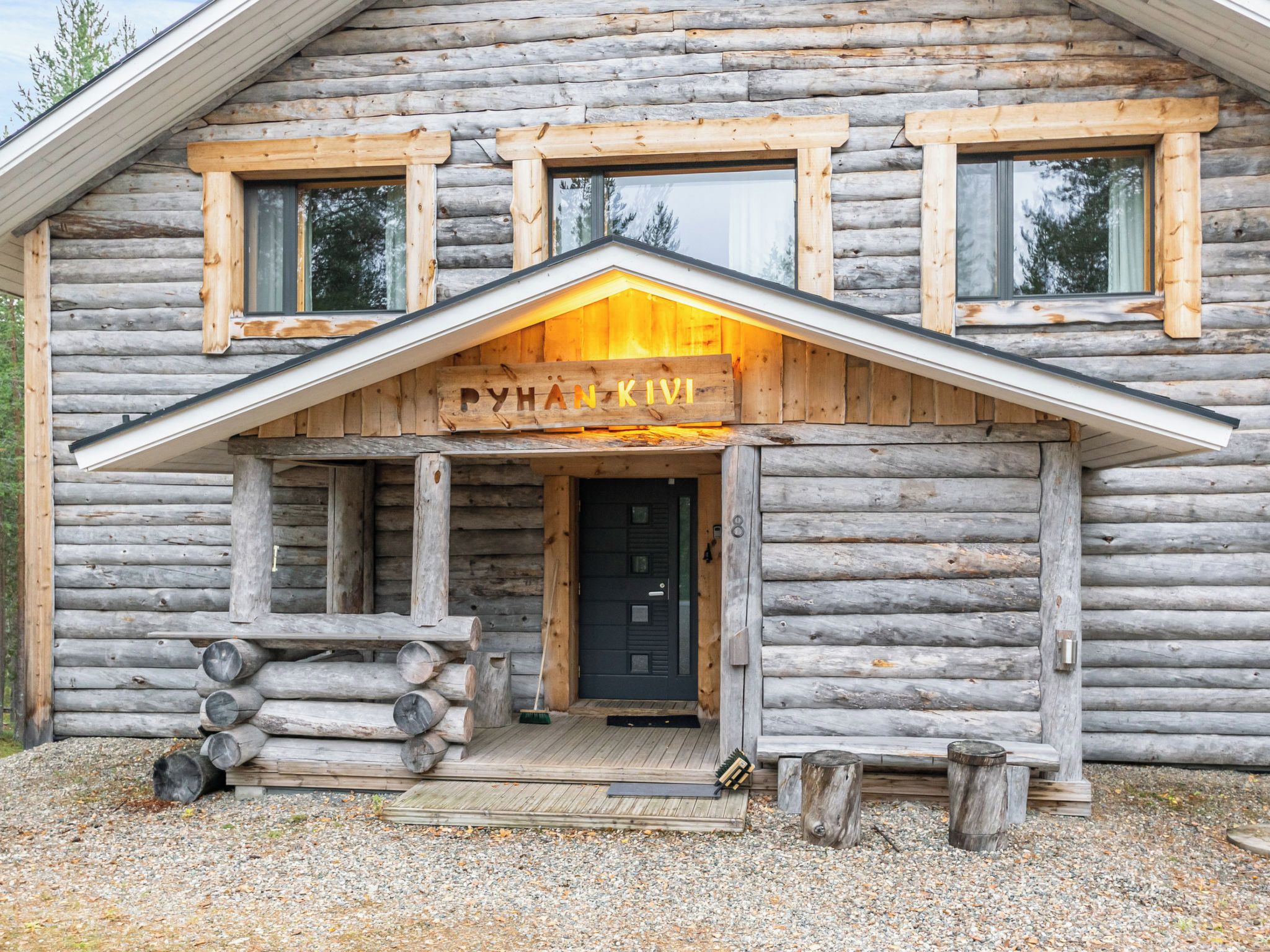Une cabane en rondins avec un porche en bois à l’avant, une porte noire et une enseigne sur laquelle on peut lire « PYHAN KIVI ».