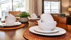 A dining table with white bowls and plates, a woven placemat, and a potted plant. - Lovely Family Home | 8-10 min to Disney (Kissimmee)
