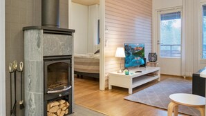 Una sala de estar acogedora con chimenea de piedra, una cama, un televisor y un ventanal con persianas.