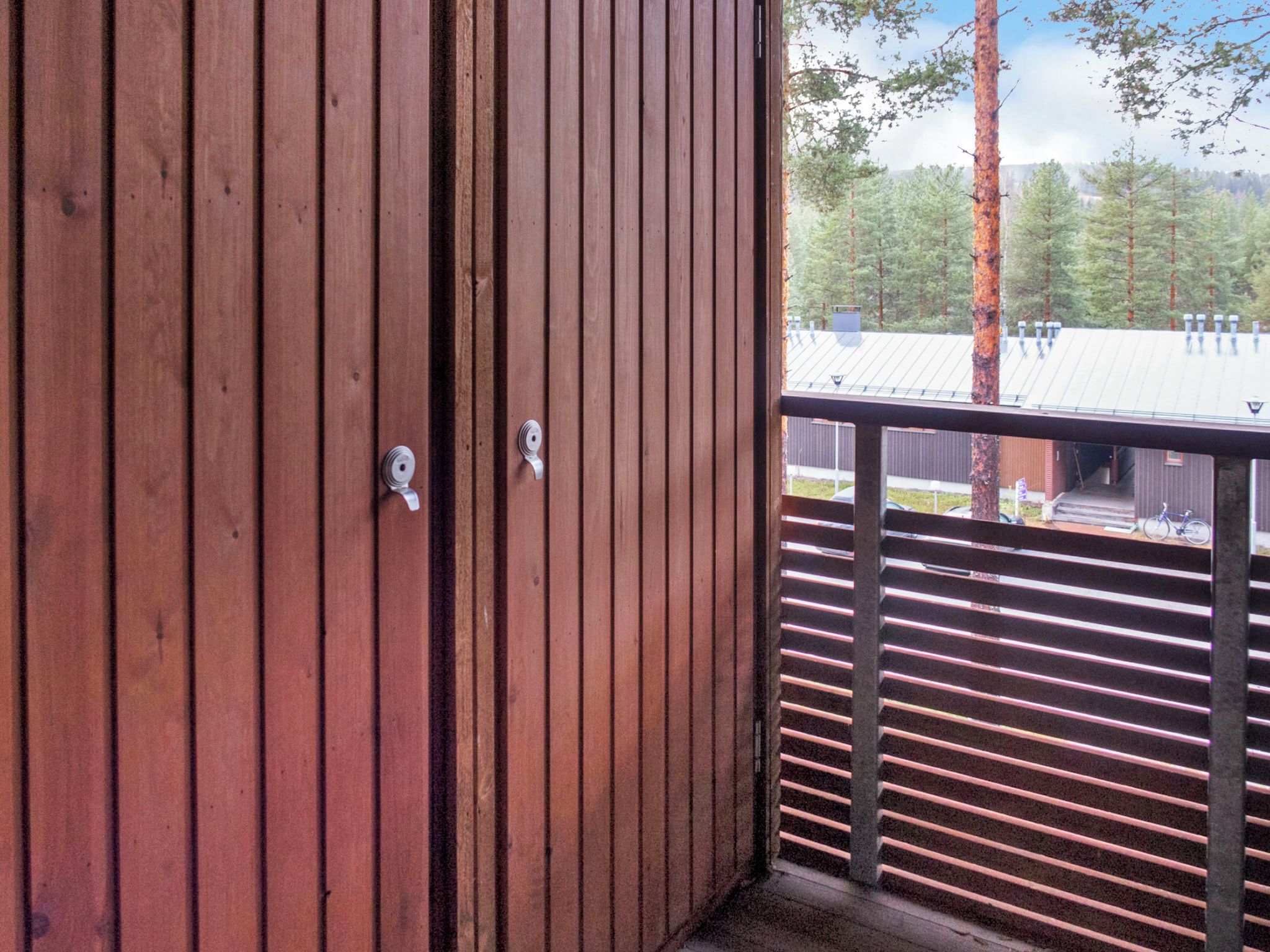 Pared exterior de madera con una puerta metálica y barandilla de balcón.