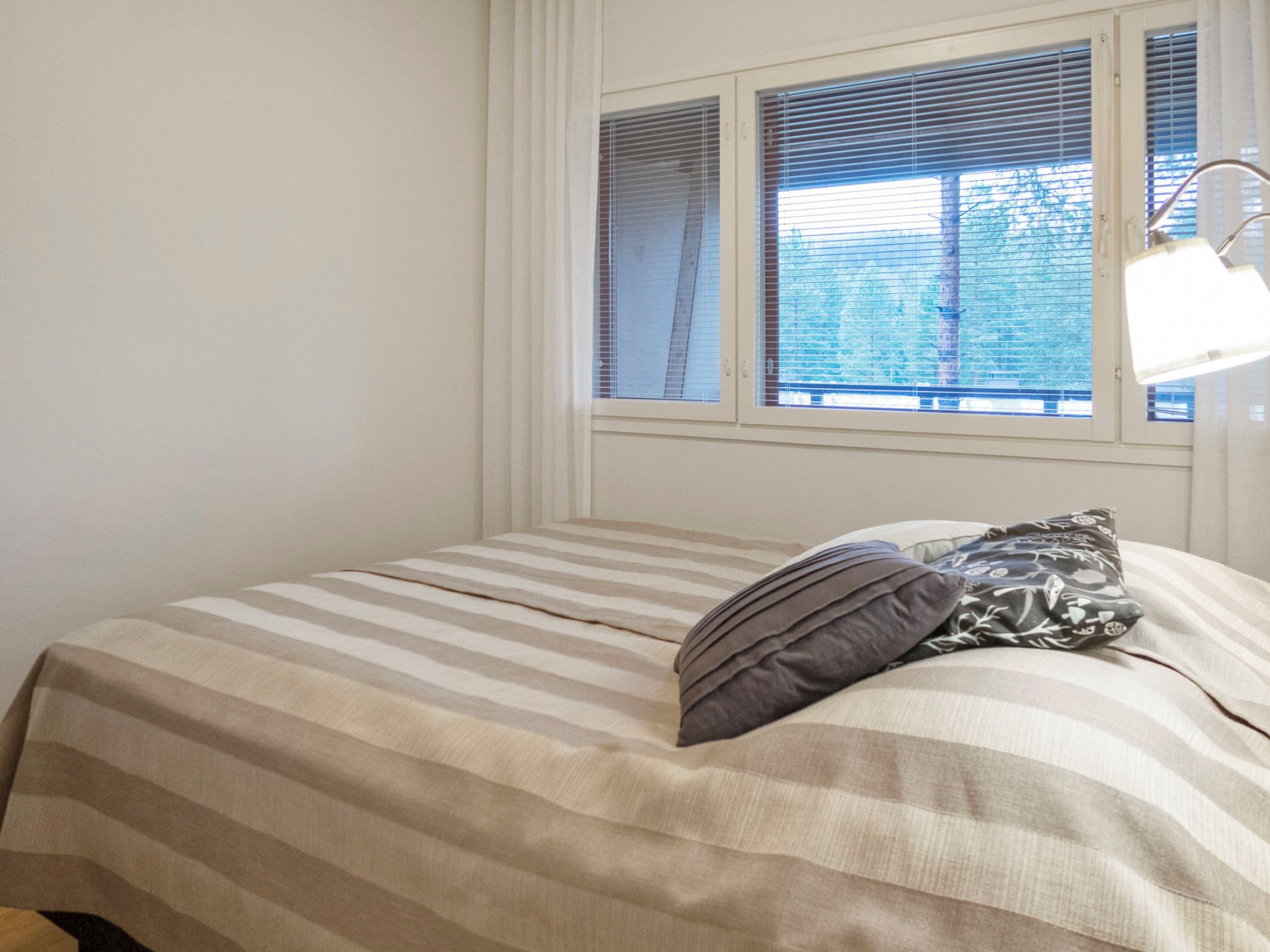 A bedroom with a bed, a window with blinds, and a bedside lamp.