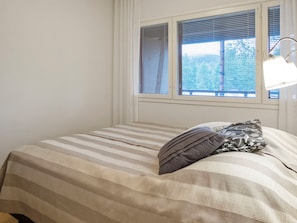 Un dormitorio con cama, ventana con persianas y lámpara de noche.