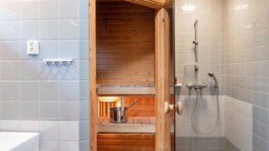 Un baño con sauna de madera, ducha y lavamanos.