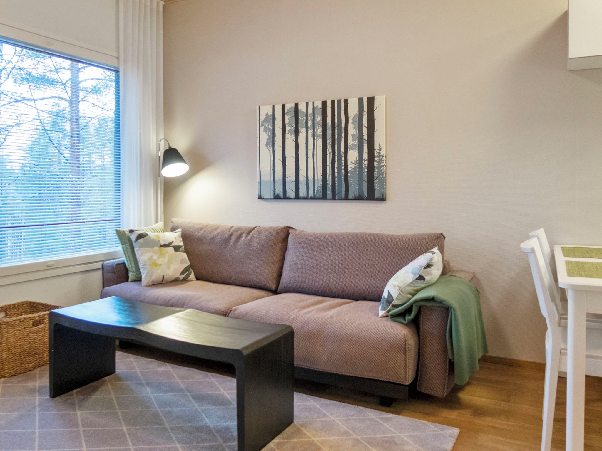 En stue med sofa, sofabord, lampe og et billede på væggen.
