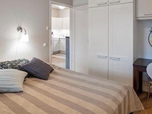 Un dormitorio con cama, almohadas, una lámpara de noche, un armario y un escritorio pequeño con una silla.