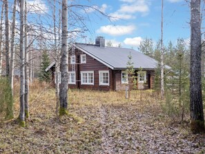 Eine zweistöckige Holz-Blockhütte mit geneigtem Dach, umgeben von Bäumen und einem mit Blättern bedeckten Boden.