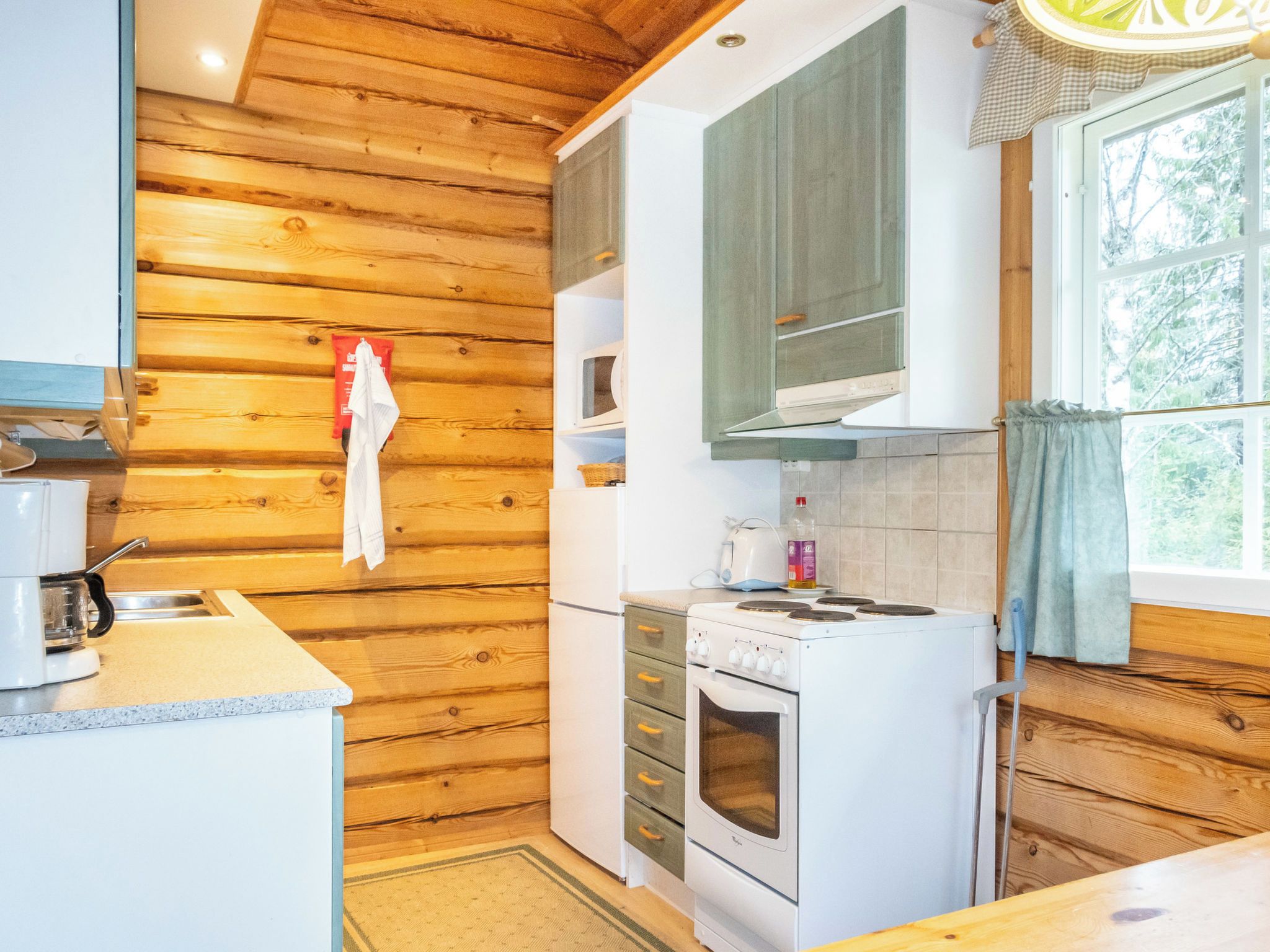 A compact kitchen with wooden walls, a white stove, and a window with curtains.