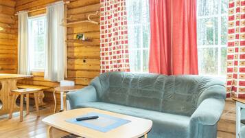 L’intérieur d’un chalet accueillant, avec un canapé, une petite table et une fenêtre agrémentée de rideaux.
