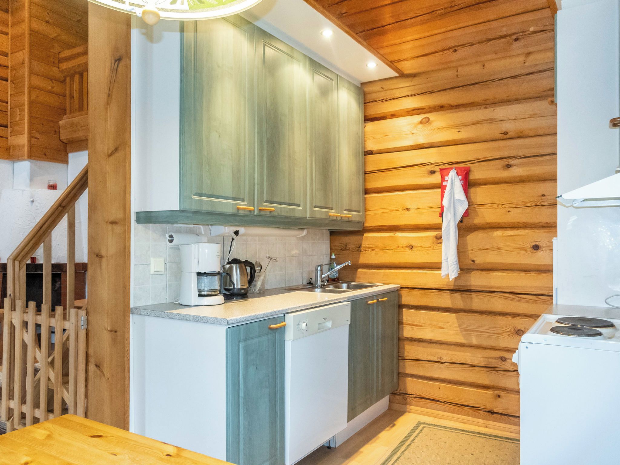 A compact kitchen with wooden walls, a built-in dishwasher, and a coffee maker.