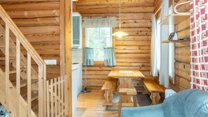 A wooden cabin interior with a dining table, benches, a sofa, and a staircase.