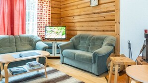 A cozy cabin interior with a wooden interior, a television, a sofa, a table, and a window with curtains.