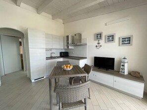 Una cocina moderna con armarios blancos, un comedor con sillas de mimbre, un televisor y decoración náutica.