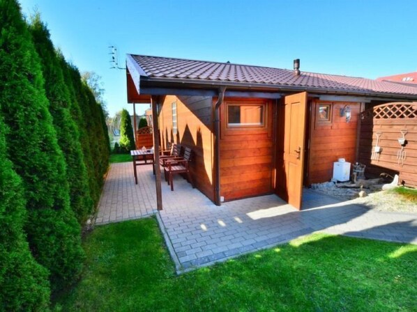Une maison en bois avec un toit en tuiles, une véranda en bois avec des bancs et un petit jardin.