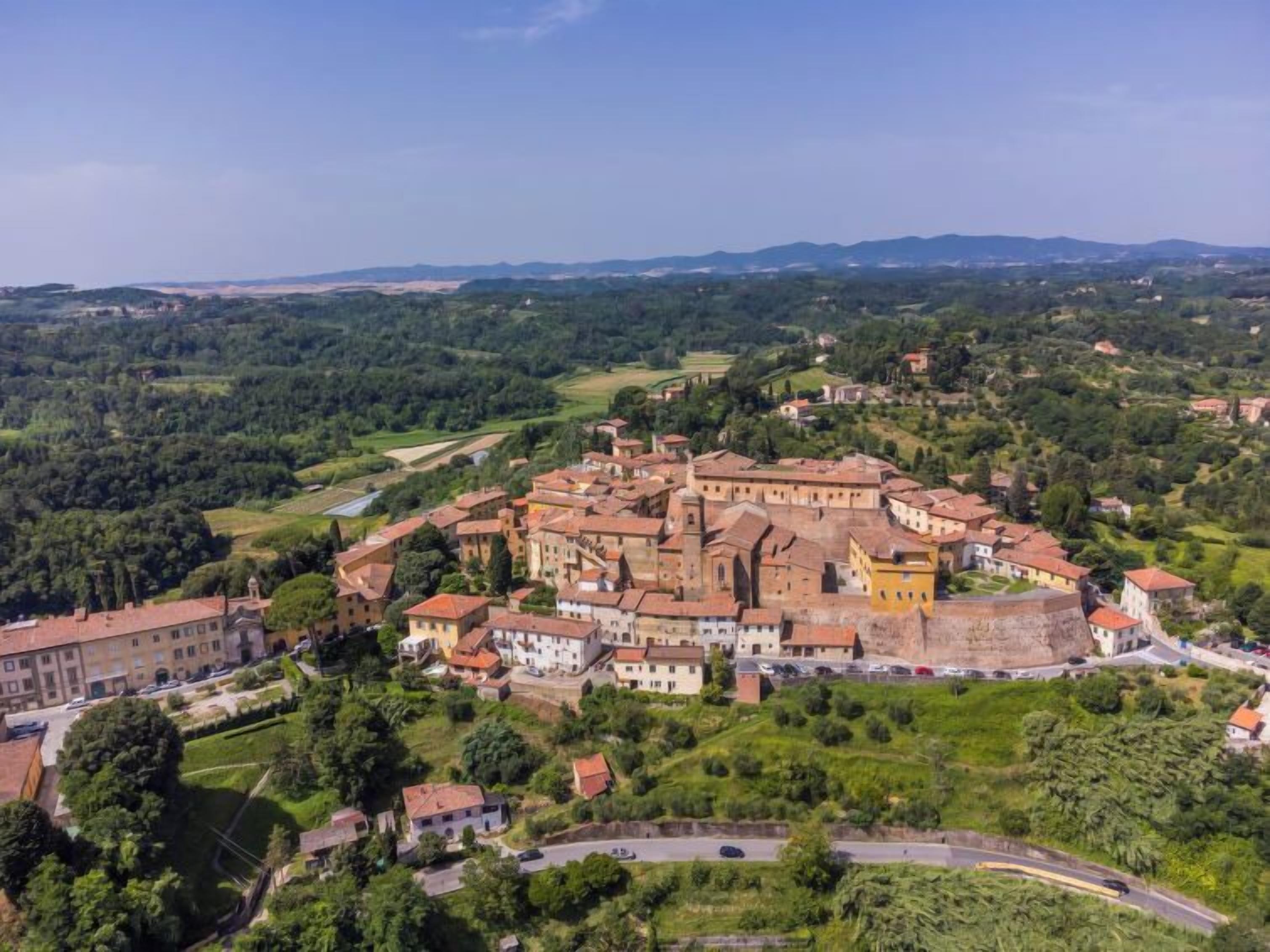 A historic town with a prominent castle-like structure surrounded by lush greenery and rolling hills.
