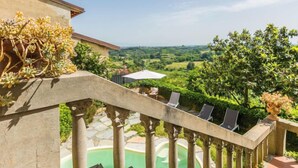 Un balcone con ringhiera in pietra, una piscina e vista su un paesaggio rigoglioso.