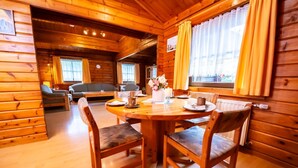 A cozy cabin interior with a wooden dining table set for four, a sofa, and a window with curtains. - Vacation home Geli by Interhome (Bad Arolsen)