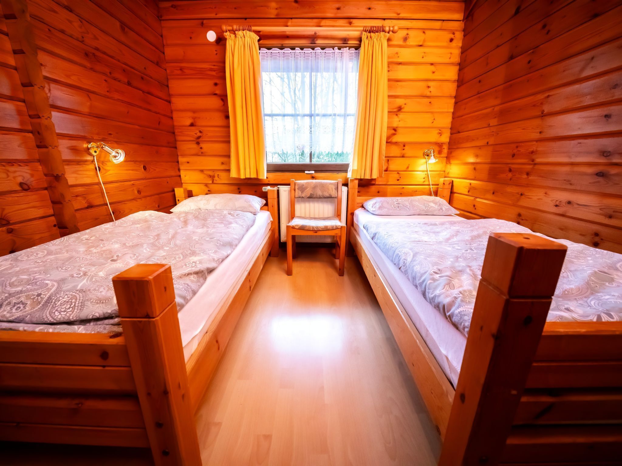 A cabin with two wooden beds, a chair, and a window with curtains.