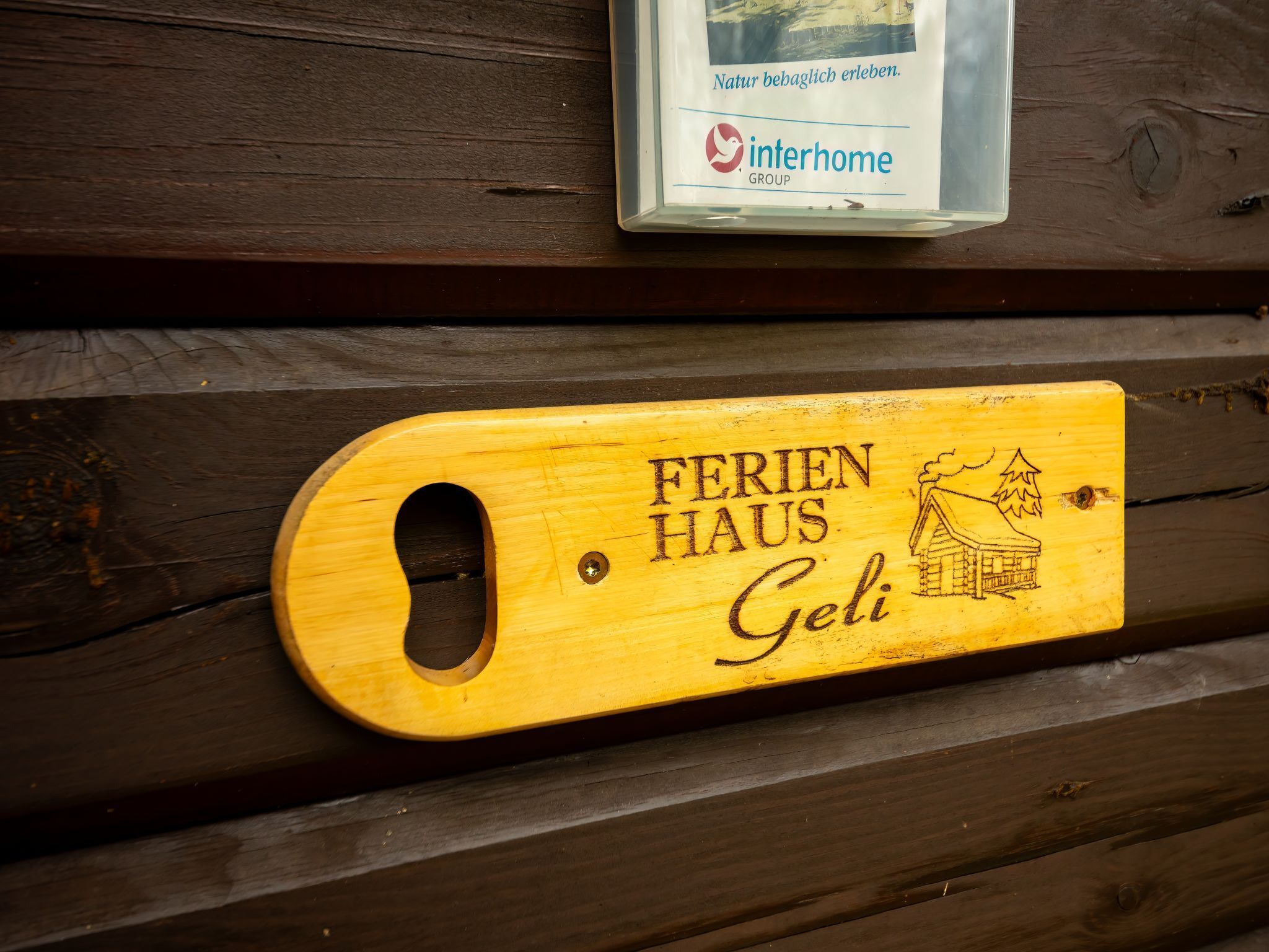 Une plaque en bois portant l’inscription « FERIEN HAUS Geli » et une petite illustration représentant une maison.