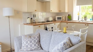 A modern kitchen with white cabinets, a microwave, and a sink. There is a dining area with a table and chairs, and a floor lamp.