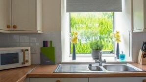 A kitchen with a window, a sink, a microwave, and a green cutting board.