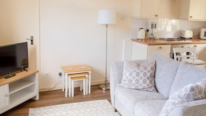 A living room with a TV, a sofa, a small table, and a lamp.