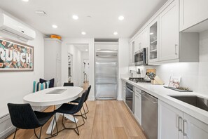 A modern kitchen with white cabinets, a stainless steel refrigerator, and a dining area with a white table and black chairs.