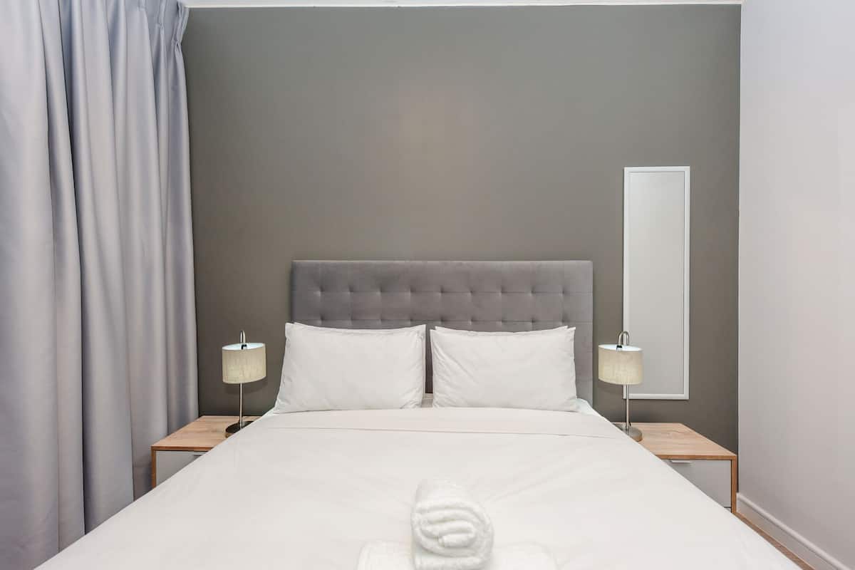 A hotel room with a large bed, two bedside tables with lamps, a grey headboard, and a large mirror on the wall.