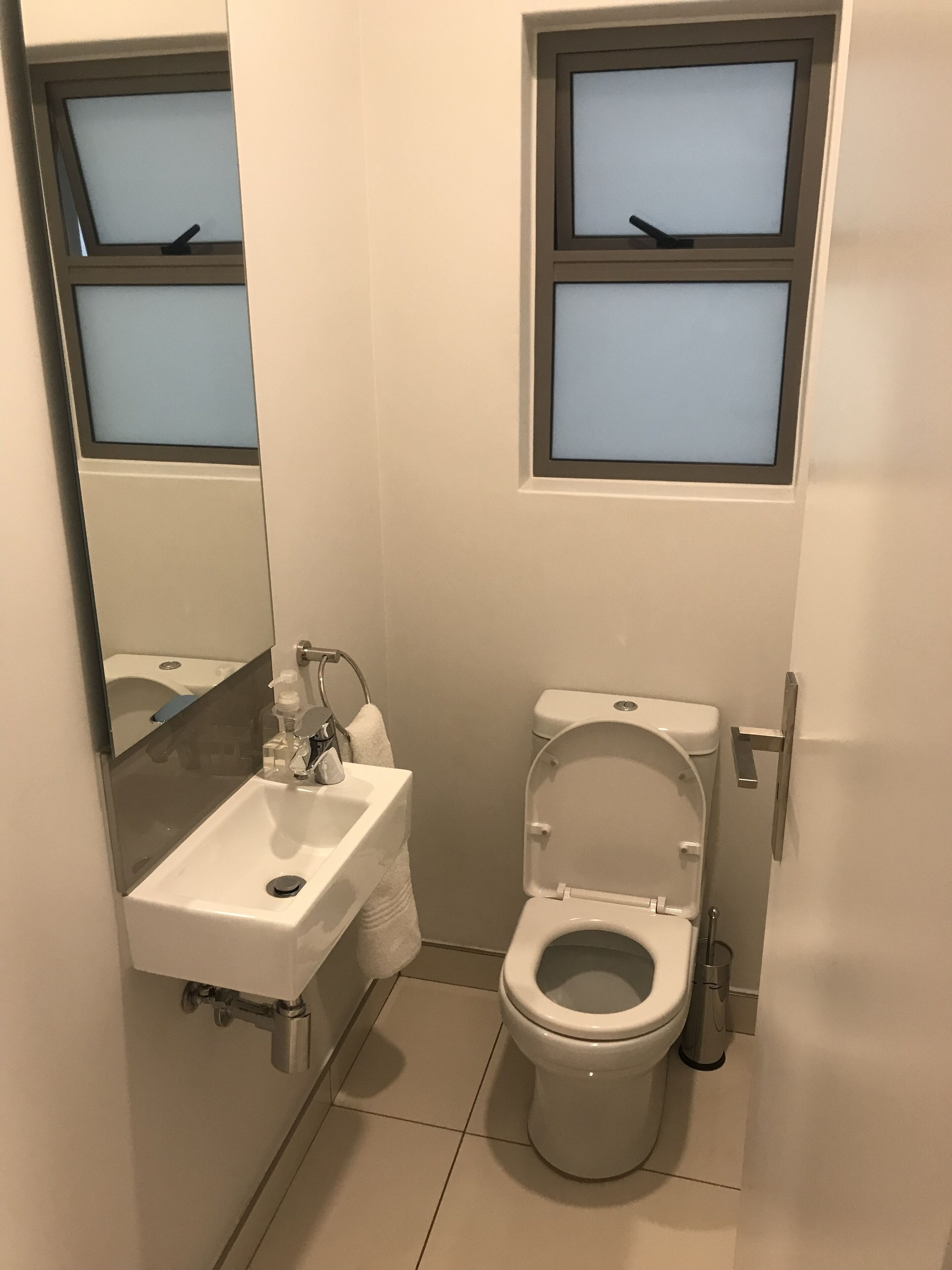 Un baño pequeño con un lavabo blanco, inodoro y una ventana sobre el inodoro.